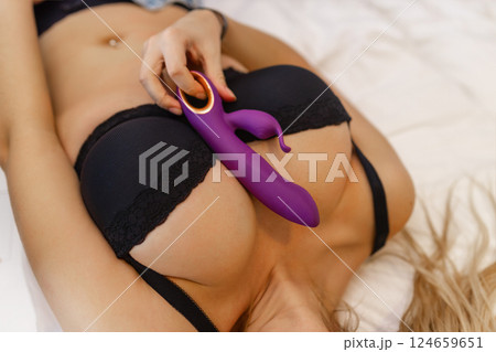 Woman in bed under sheets holding vibrator in hand 124659651