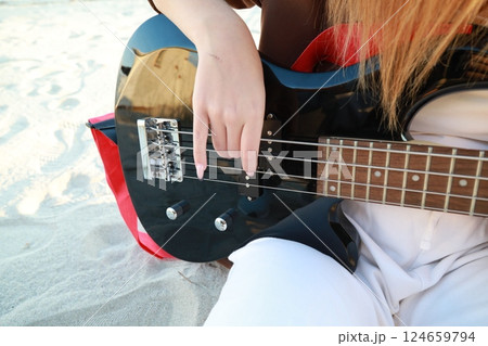 Girl Plays The Bass Instrument Sitting On The Beach At Sunset Near The Ocean Girl Plays The Bass Instrument Sitting On The Beach At Sunset Near The Ocean 124659794