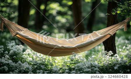 Relaxing beige hammock hangs between trees in a sun-dappled forest, surrounded by blooming white wildflowers 124660428