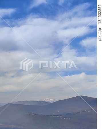 Snowy mountaintops rise above layers of dark hills and scattered villages. The contrast between fog, sky, and mountains creates a dramatic natural composition. Snowy mountaintops rise above layers of dark hills and scattered villages. The contrast between fog, sky, and mountains creates a dramatic natural composition. 124662886
