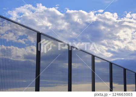 High security fence reflecting clouds and blue sky High security fence reflecting clouds and blue sky 124663003