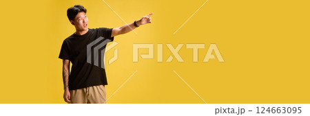 Energetic young man in casual outfit pointing away with excitement against yellow backdrop. Concept of holiday vibe. Energetic young man in casual outfit pointing away with excitement against yellow backdrop. Concept of holiday vibe. 124663095