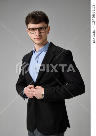 Mid-length shot of stylish young man adjusting jacket, standing confidently, showing elegance. Concept of fashion, leadership Mid-length shot of stylish young man adjusting jacket, standing confidently, showing elegance. Concept of fashion, leadership 124663115