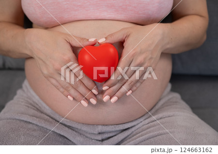 Caucasian pregnant woman holding heart on belly background. Third trimester. Caucasian pregnant woman holding heart on belly background. Third trimester. 124663162
