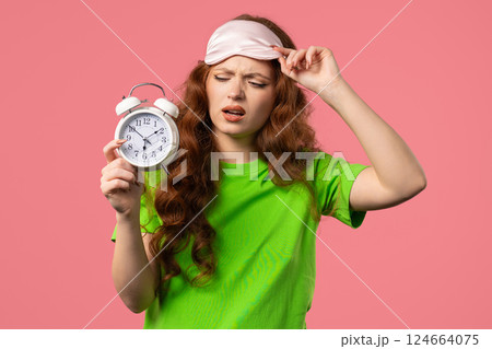 Woken up by alarm clock sleepy young woman holding it in hand. pink background 124664075