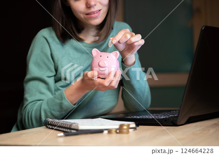 The girl puts her savings in a piggy bank. 124664228
