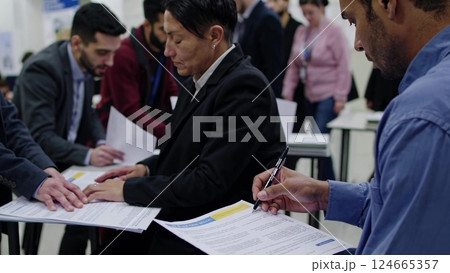 Applicants Filling Forms in Busy Migration Center Applicants Filling Forms in Busy Migration Center 124665357