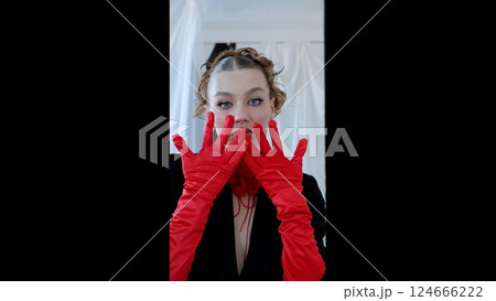 Elegant woman wearing vivid red gloves and sleek black dress, striking dramatic pose against minimalist backdrop, highlighting haute couture styling with confident demeanor 124666222