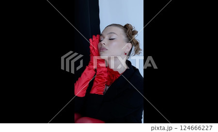 Glamorous studio portrait featuring elegant woman draped in black dress, long crimson gloves, dramatic makeup highlighting sophisticated style 124666227