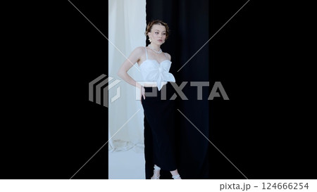 Fashion model wearing white top and black skirt, standing confidently in studio with monochromatic backdrop, representing contemporary style and sophisticated elegance 124666254