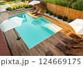 Stylish backyard with turquoise swimming pool, wooden deck, lounge chairs, and white umbrellas 124669175