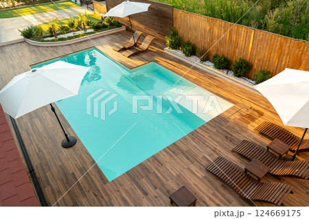 Stylish backyard with turquoise swimming pool, wooden deck, lounge chairs, and white umbrellas Stylish backyard with turquoise swimming pool, wooden deck, lounge chairs, and white umbrellas 124669175