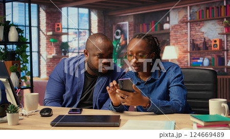 African american man and woman solving freelance tasks at home, working together on their phones to finish an important project for their employer. Networking with partners. Camera A. 124669489