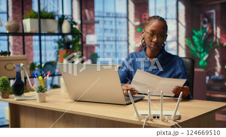 Irritated African American girl struggling to reach the internet provider to help fix the signal loss issues, freelancer working at home with an unstable Wi Fi connection. Camera A. Irritated African American girl struggling to reach the internet provider to help fix the signal loss issues, freelancer working at home with an unstable Wi Fi connection. Camera A. 124669510