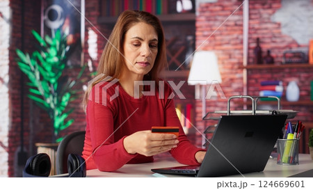 Casual woman staying at home and paying for things online on laptop, entering credit card digits to confirm payment and make purchase. Mature person does online shopping in loft. Camera A. Casual woman staying at home and paying for things online on laptop, entering credit card digits to confirm payment and make purchase. Mature person does online shopping in loft. Camera A. 124669601
