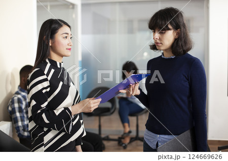 Recruiter inviting female candidate to join agency team for employment meeting. Asian woman preparing for career opportunity, hands her resume to caucasian HR manager in startup office waiting area. Recruiter inviting female candidate to join agency team for employment meeting. Asian woman preparing for career opportunity, hands her resume to caucasian HR manager in startup office waiting area. 124669626
