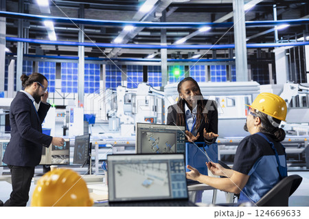 Solar panels plant engineering team doing quality control using computer, ensuring high efficiency. Photovoltaics factory teamworking colleagues calibrating assembly lines robotic arms Solar panels plant engineering team doing quality control using computer, ensuring high efficiency. Photovoltaics factory teamworking colleagues calibrating assembly lines robotic arms 124669633