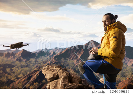 Young explorer influencer recording aerial view vlog with his drone, enjoying the fresh air on mountain range valley. Content creator hiker filming his latest travel vlog, exploration. 124669635