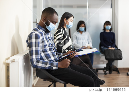 Multicultural applicants gathers in lobby area for HR interviews, reading recruitment documents. Diverse candidates holding resumes, waiting in office queue for job hiring meeting. 124669653