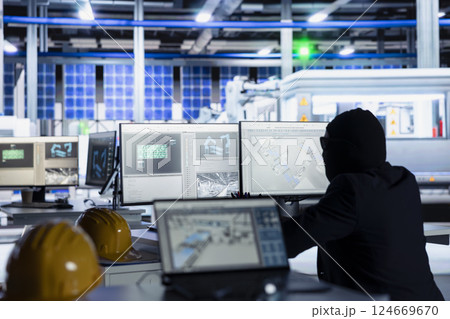 Masked worker in photovoltaics factory commits corporate espionage, looking over blueprints on PC, stealing proprietary technology. Man bypasses solar panel plant security to copy trade secrets 124669670