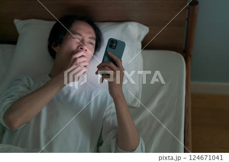 ベッドの中でスマホを操作する男性 124671041