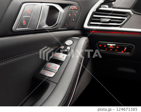 Door handle with power window control buttons. Black perforated leather interior with stitching. Modern car black leather interior details. Door handle with power window control buttons. Black perforated leather interior with stitching. Modern car black leather interior details. 124671385