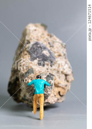 A tiny figurine of a man pushing a massive rock, symbolizing perseverance, struggle, and determination. 124671514