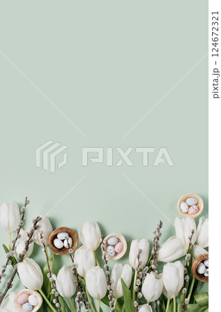 Creative Easter flat lay featuring white tulips, speckled pastel eggs in nests, pussy willow branches, and soft feathers on mint green background. space for festive advertisements Creative Easter flat lay featuring white tulips, speckled pastel eggs in nests, pussy willow branches, and soft feathers on mint green background. space for festive advertisements 124672321