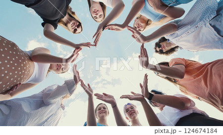 Group of students making a circle with their hands against a blue sky, demonstrating teamwork, friendship, and unity 124674184