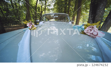 White vintage car decorated with flower bouquets and ribbons, parked in a forest, ready for a wedding ceremony 124674232