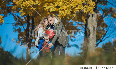 Family walking together through autumn park, golden leaves falling, sharing warm smiles and embracing seasonal beauty 124674287