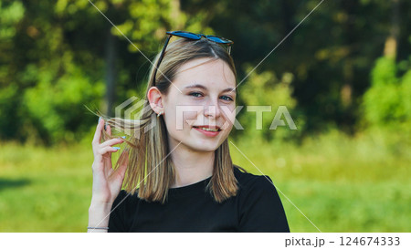 Smiling blonde teenage student girl playing with her hair in a sunny park on a summer day Smiling blonde teenage student girl playing with her hair in a sunny park on a summer day 124674333