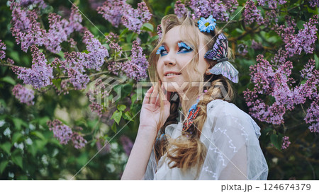 Elegant model wearing colorful butterfly accessories, posing near lilac blossoms with vivid makeup, capturing springtime essence 124674379