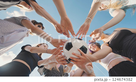 Group of young women forming a circle around a soccer ball with their hands, viewed from a low angle. Group of young women forming a circle around a soccer ball with their hands, viewed from a low angle. 124674382