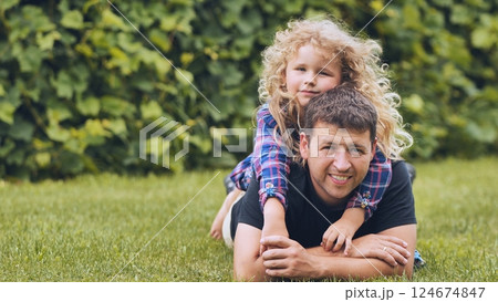 Father and daughter lying together on sunlit grass, sharing laughter and tender connection during outdoor family moment 124674847
