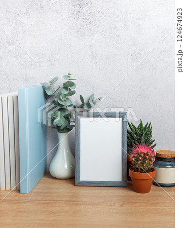 Blue picture frame standing on wooden desk with plants and books behind 124674923