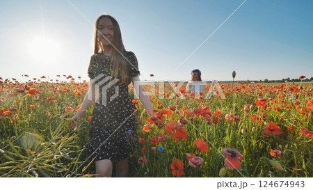 Ukrainian girls strolling through vibrant red poppy field, basking in warm golden evening sunlight 124674943