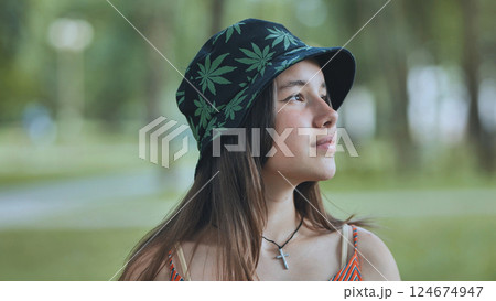 Portrait of a contemplative teenage girl wearing a bucket hat with cannabis leaf design, enjoying a summer day in a park Portrait of a contemplative teenage girl wearing a bucket hat with cannabis leaf design, enjoying a summer day in a park 124674947