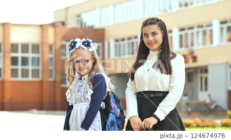 Schoolgirl hugging mother, beaming beside school entrance during back to school moment 124674976