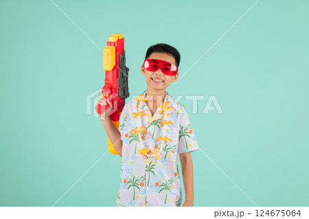Songkran celebration as a joyful Thai child in glasses and a floral shirt holds a water gun 124675064