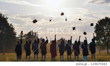 Group of students in academic gowns joyfully throwing graduation caps into the air during a vibrant sunset, celebrating their achievements together Group of students in academic gowns joyfully throwing graduation caps into the air during a vibrant sunset, celebrating their achievements together 124675083