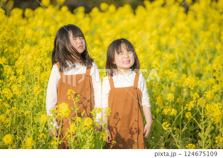 菜の花に囲まれて春を楽しむ姉妹 124675109