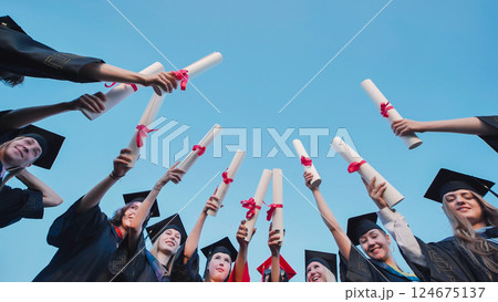 Happy students in graduation gowns proudly holding up their diplomas 124675137