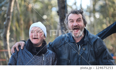 Intoxicated homeless pair grinning, revealing toothless grins amid snowy woodland landscape 124675253