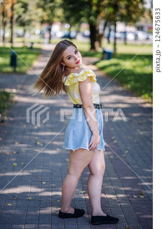 Stylish woman strolling across sunlit park, embracing warm daylight and breathing fresh summer atmosphere 124675633
