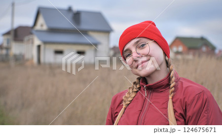 Cheerful teenage girl wearing red beanie and braids, smiling confidently with blurred suburban backdrop 124675671