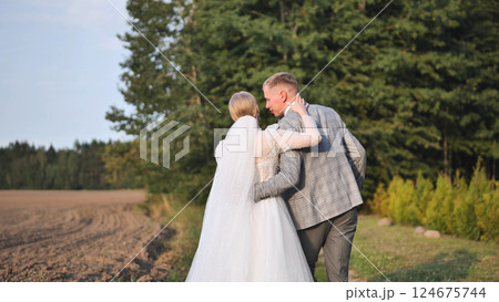 Newlywed couple strolling together, holding hands in sunlit meadow, sharing intimate wedding day moment Newlywed couple strolling together, holding hands in sunlit meadow, sharing intimate wedding day moment 124675744
