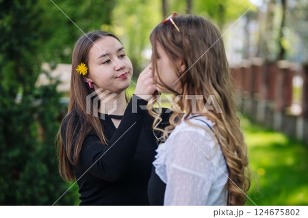 Schoolgirl helping her friend with her hair using a dandelion on a lovely spring day at school 124675802