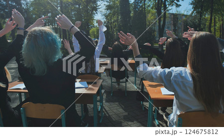 Happy students raising their hands at outdoor desks, celebrating the end of the school day Happy students raising their hands at outdoor desks, celebrating the end of the school day 124675812