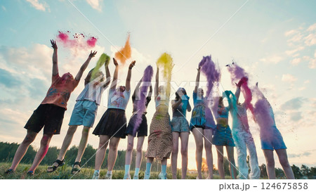 Cheerful school friends celebrating together by throwing colorful holi powder in the air during sunset 124675858